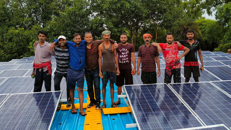 Group of men standing on roof around solar panels.